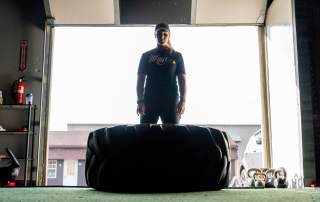athlete working out with large tire in front of open garage door